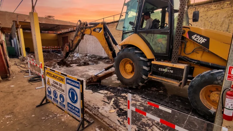Retroexcavadora trabajando en la demolición controlada de un local comercial, con señalización de zona de demolición