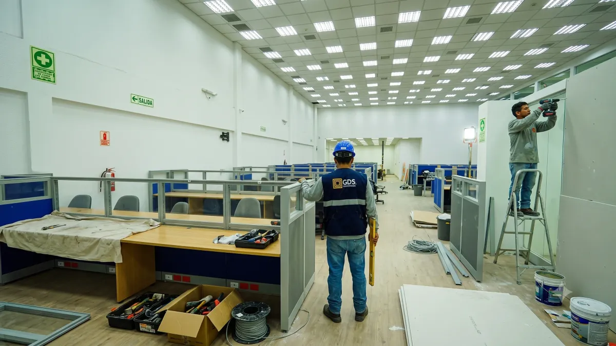 Cuadrilla de GDS montando mamparas y mobiliario en una oficina corporativa, con señalización de zona de remodelación